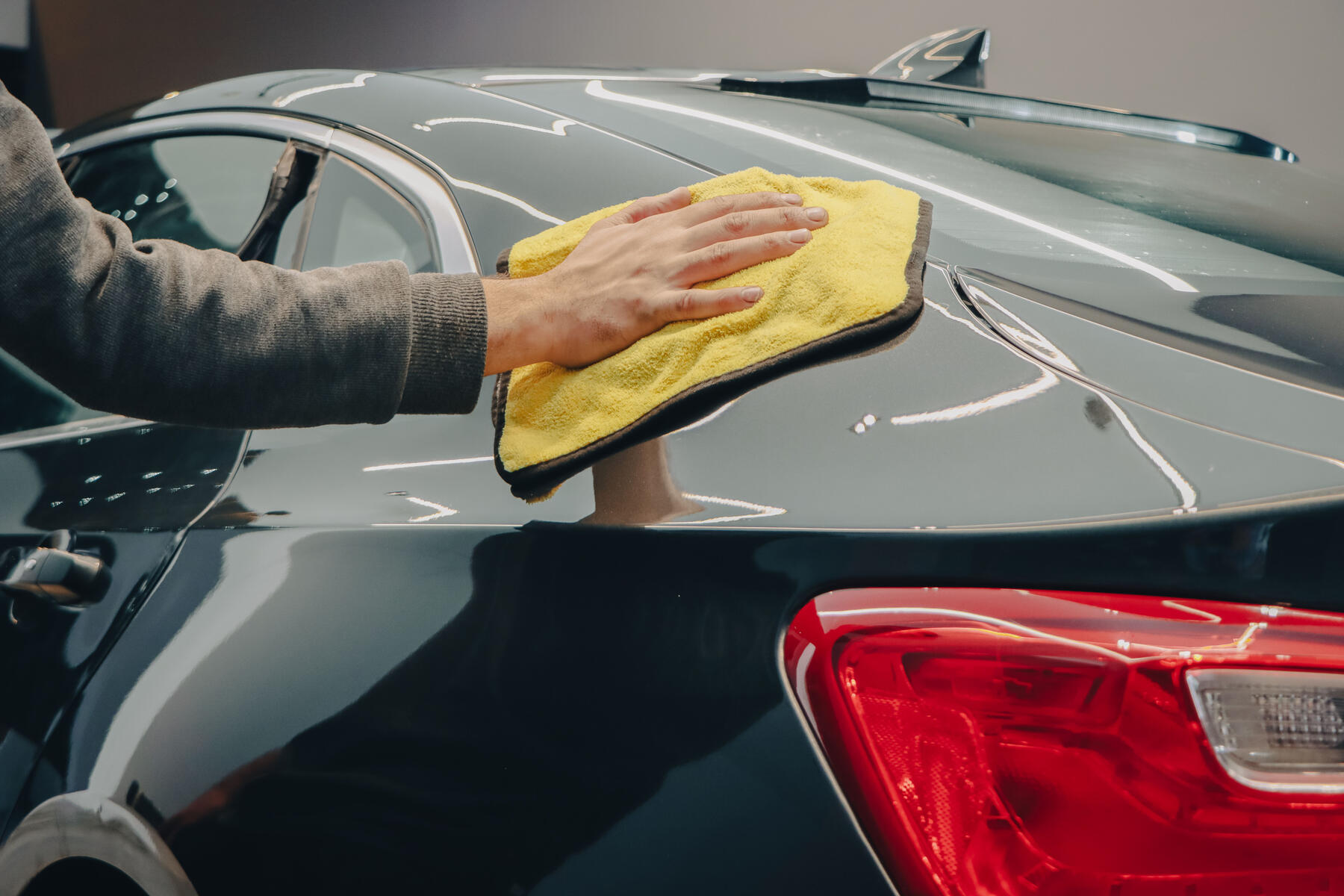Careful Exterior Detailing Detailer wiping a black vehicle exterior with a yellow microfiber towel